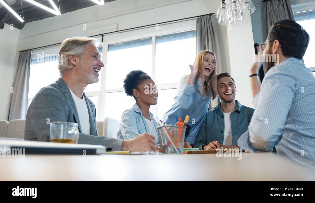 Due giovani uomini d'affari allegri che danno cinque alti mentre i loro colleghi li guardano e sorridono. Il team aziendale festeggia il successo Foto Stock