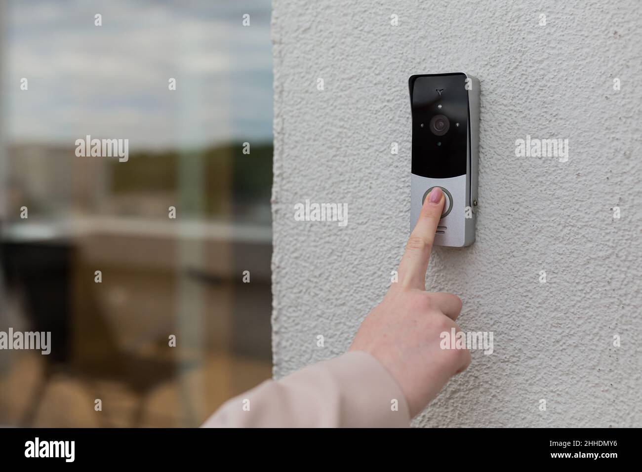 la mano della donna usa un campanello sulla parete della casa con una macchina fotografica di sorveglianza Foto Stock