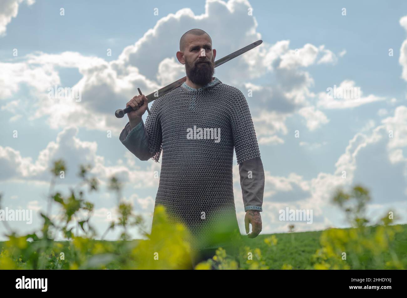 L'uomo calvo portava in metallo a catena posta sopra la camicia di lino si alza in mezzo al campo, tenendo la spada. Aspetto militante. Sfondo sfocato. Foto Stock