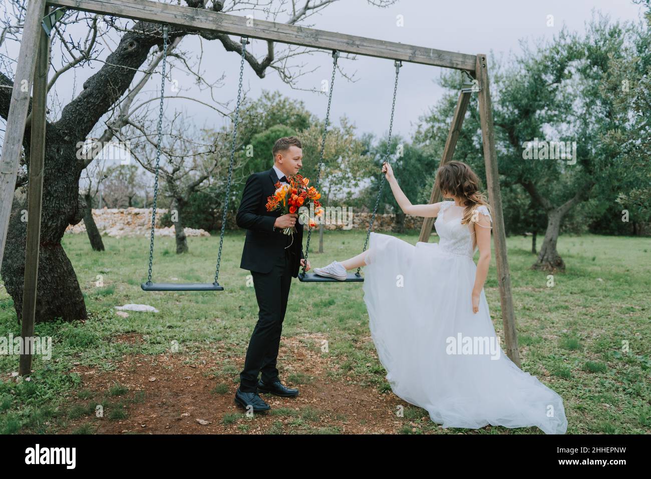 Felice coppia sorridente di stile che cammina in Toscana, Italia il giorno del matrimonio. SPOSI NOVELLI CON L'ALTALENA NEL PARCO. La sposa e lo sposo camminano giù il Foto Stock