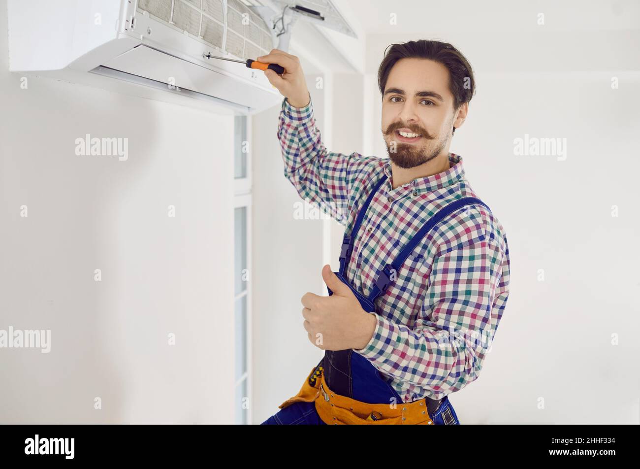 Tecnico professionale maschile che mantiene i moderni condizionatori d'aria all'interno. Foto Stock