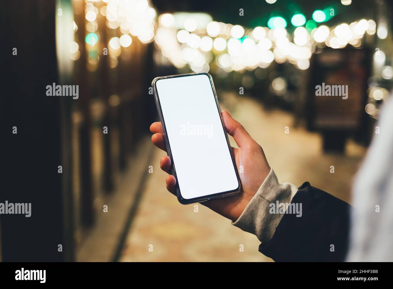 Femmina che tiene in mano moderno smartphone con display vuoto su strada città illuminata di notte Foto Stock