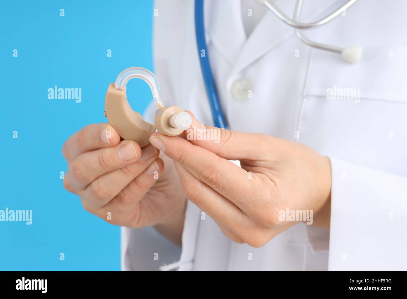 Medico che tiene un apparecchio acustico su sfondo blu Foto Stock