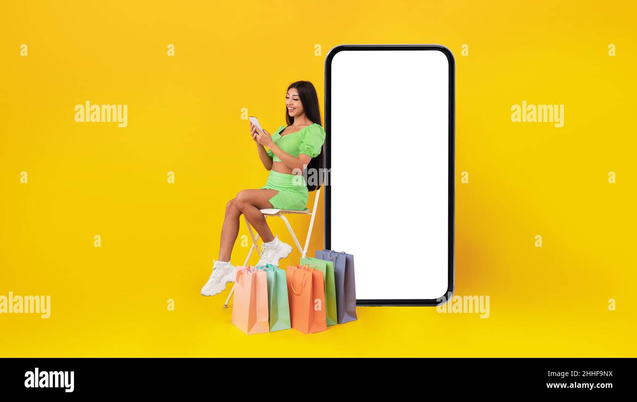 Signora felice con i sacchetti di shopping seduti vicino al telefono cellulare schermo Foto Stock