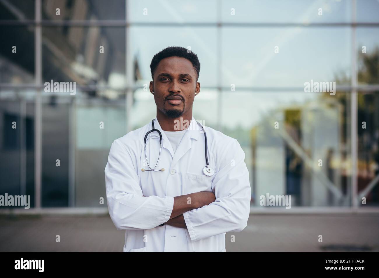Ritratto di un giovane medico afroamericano serio, vicino alla clinica, in un abito medico bianco guardando la macchina fotografica Foto Stock