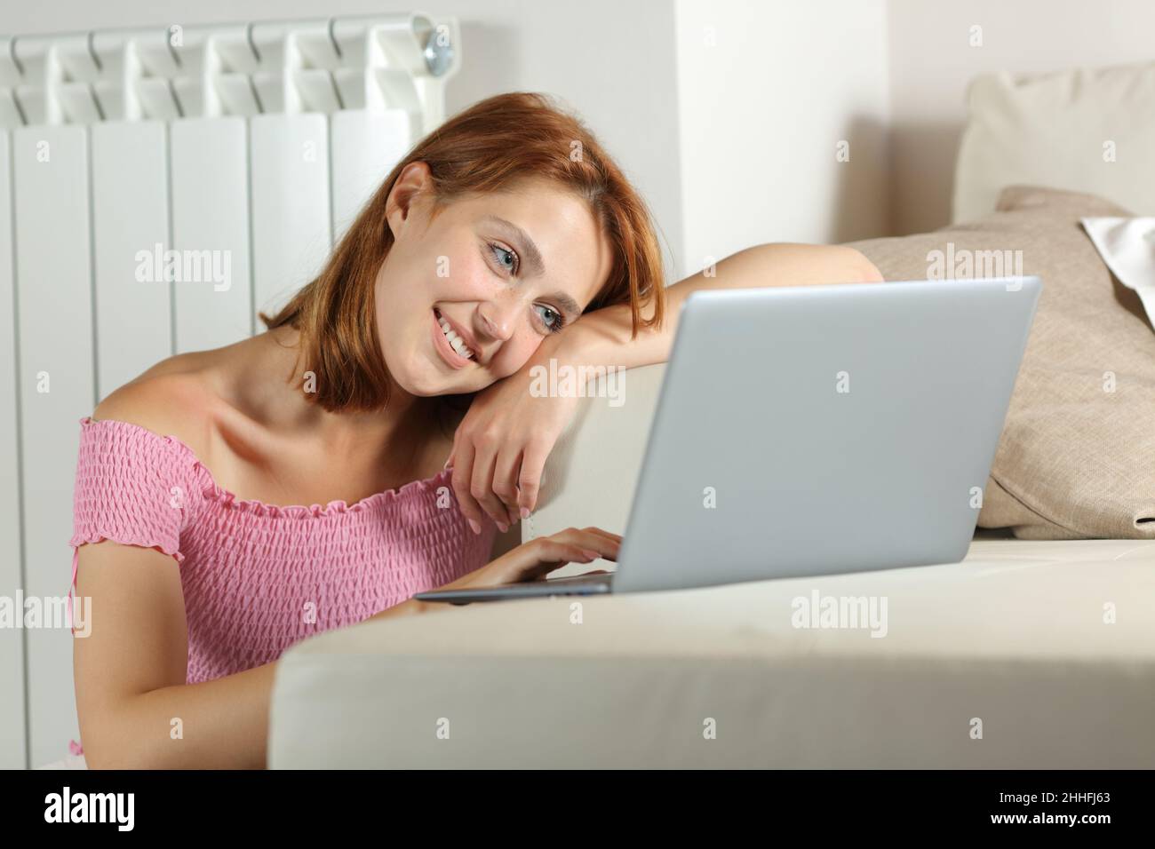 Donna felice che guarda i media su un portatile seduto in una casa interna Foto Stock