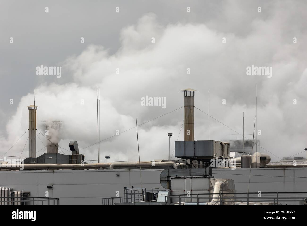 Spruzzi di vapore che fuoriescono dai camini sul tetto di un impianto industriale. Foto scattata in una giornata nuvolosa, con luce uniforme e morbida. Foto Stock