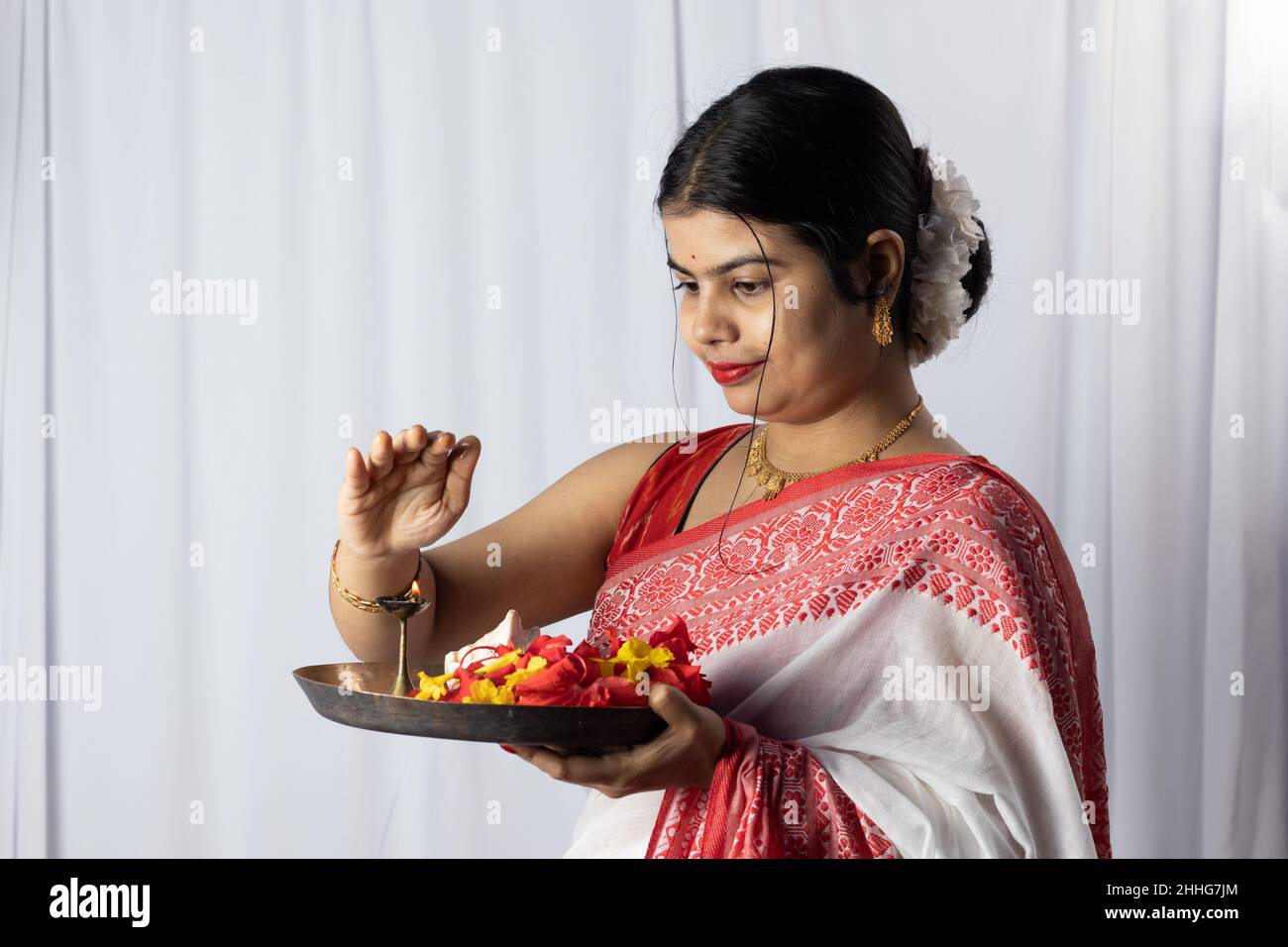 Una bella donna indiana in rosso saree tenendo puja thali o piatto di preghiera su sfondo bianco Foto Stock