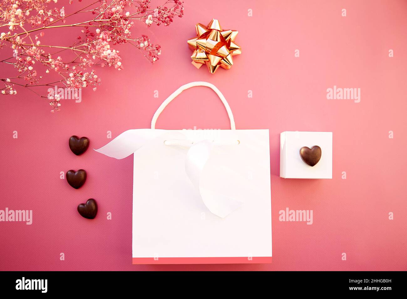 Borsa regalo bianca e caramelle al cioccolato a forma di cuore. White box idea regalo creativo. Vista dall'alto. Cena romantica. Sfondo rosa e fiore di gypsofila. Foto di alta qualità Foto Stock