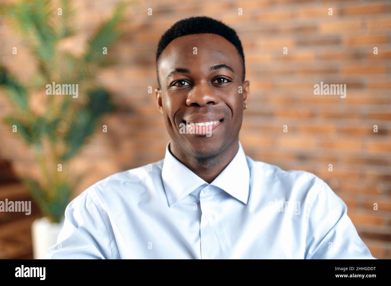 Primo piano di un bel uomo d'affari afroamericano sorridente, proprietario di piccola impresa, dirigente aziendale o direttore delle vendite, agente immobiliare di successo, in un ufficio moderno, guardando la macchina fotografica, sorridendo Foto Stock