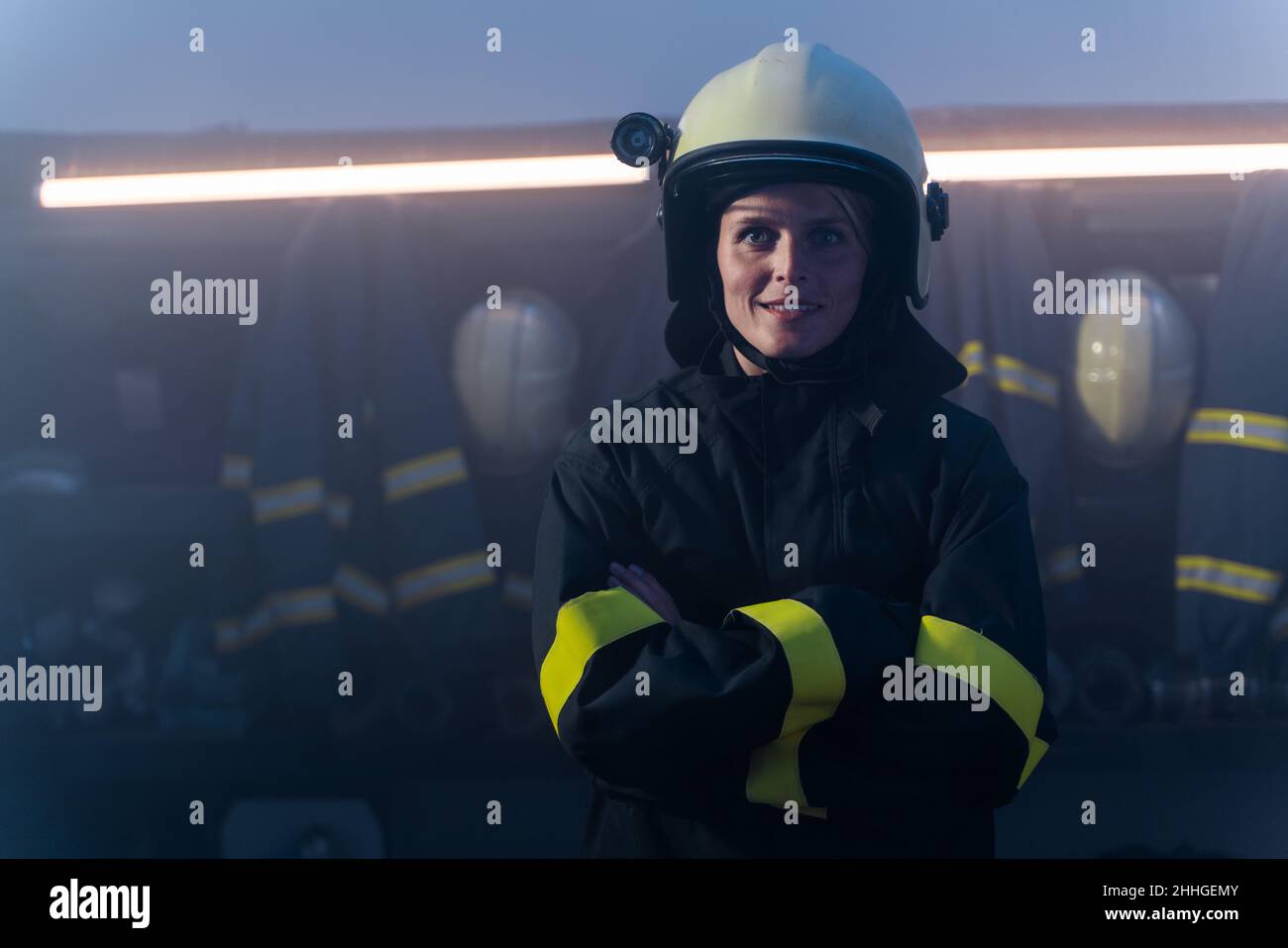Felice metà adulto femmina vigile del fuoco guardando la macchina fotografica all'interno della stazione dei vigili del fuoco di notte. Foto Stock
