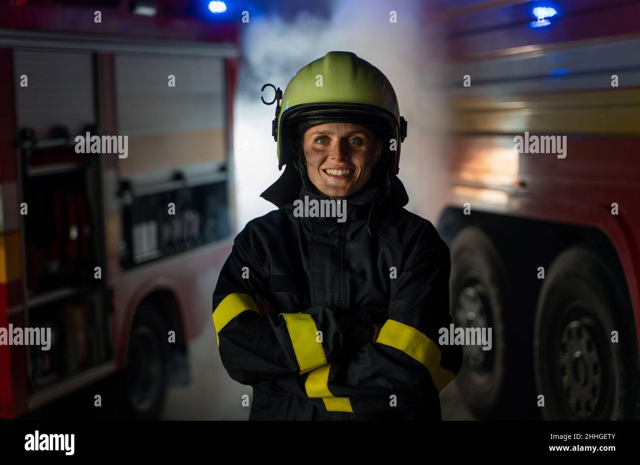 Felice donna sporca vigile del fuoco guardando la macchina fotografica con camion del fuoco sullo sfondo di notte. Foto Stock