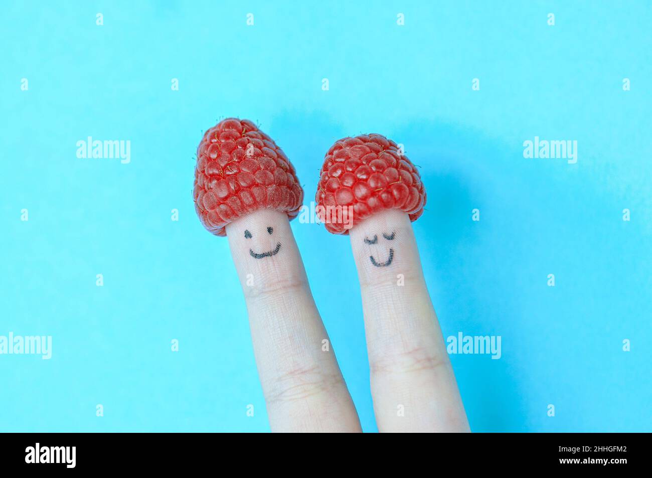 Due dita con sorrisi e lampone come cappello. Sfondo blu. Foto Stock