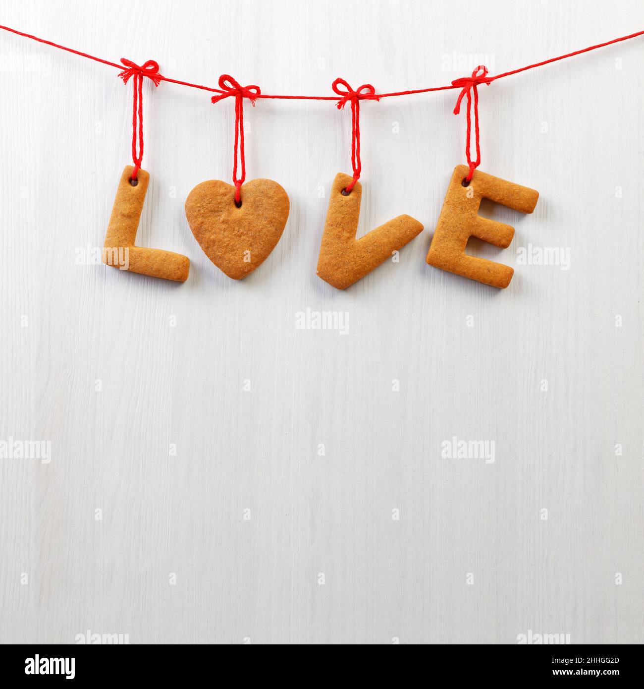 Biscotti fatti in casa di pan di zenzero a forma di cuore e lettere 'AMORE' appesi su uno sfondo bianco di legno. CopySpace. Foto Stock