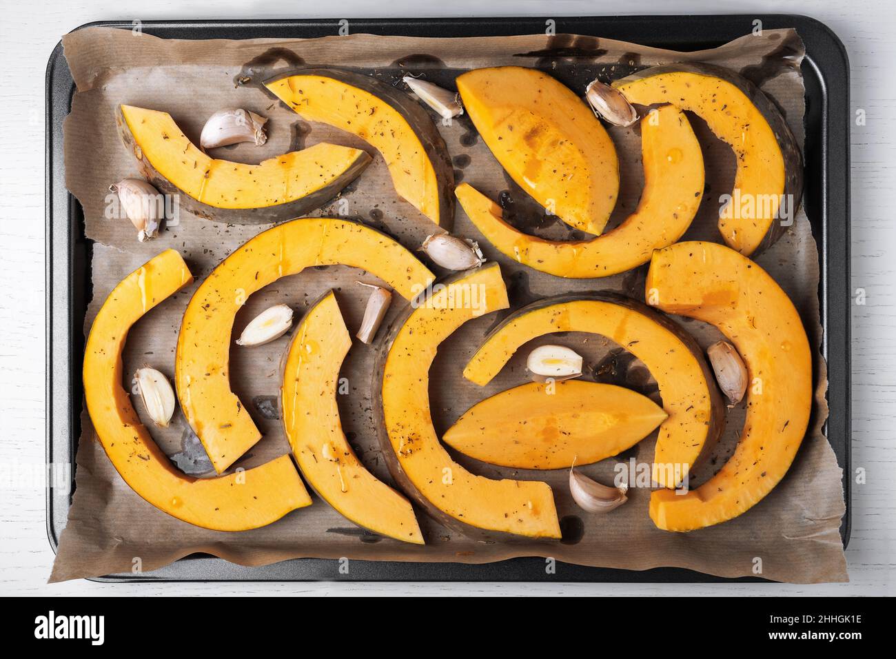 Grandi pezzi di zucca sono disposti su carta pergamena su foglio da forno con olio d'oliva, aglio ed erbe secche. Cibo sano e vegetariano. Selettivo f Foto Stock