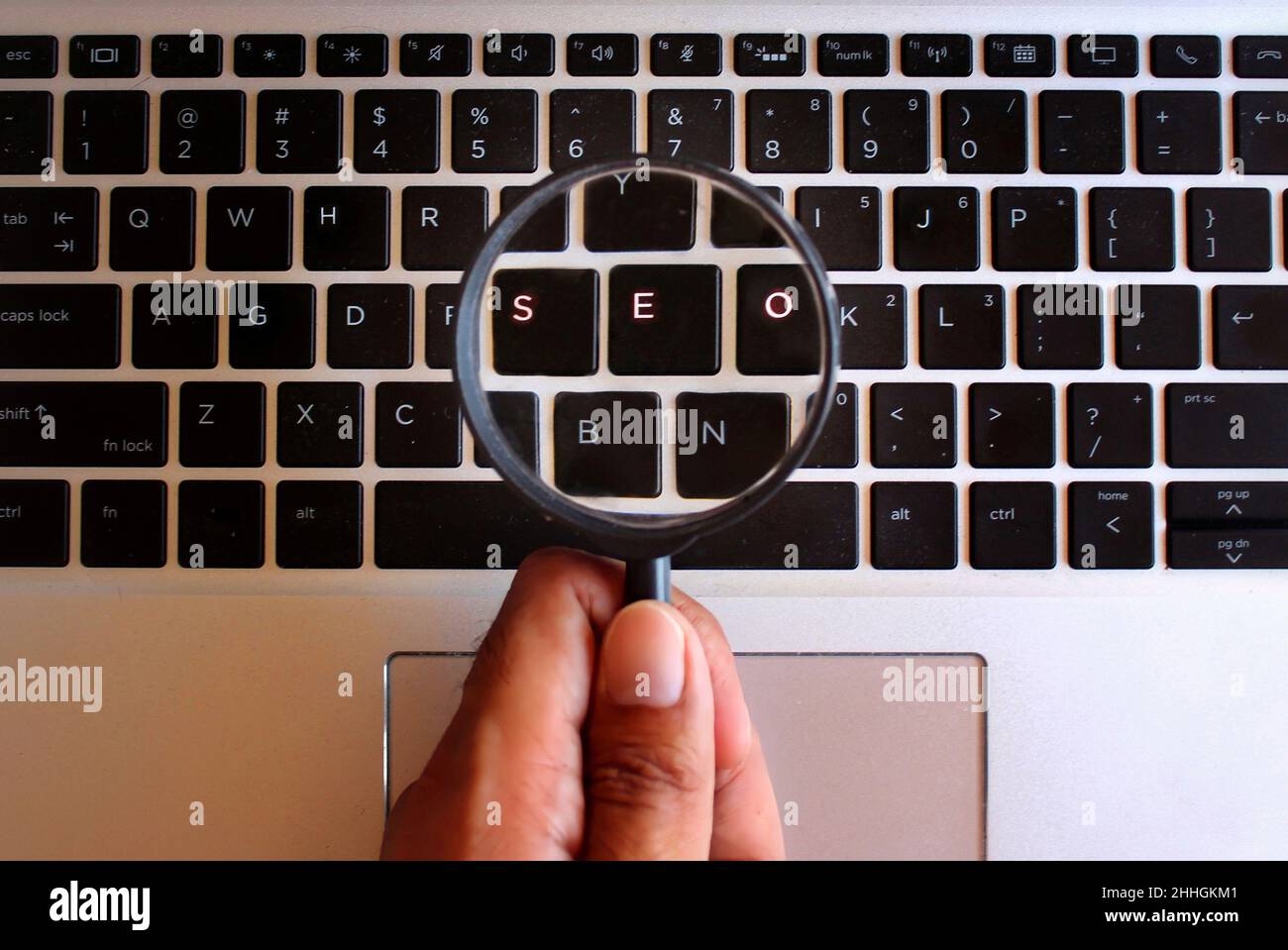 Immagine di messa a fuoco selettiva di una lente di ingrandimento e di una tastiera luminosa con testo SEO. Ottimizzazione di Search Engine o concetto di SEO. Foto Stock