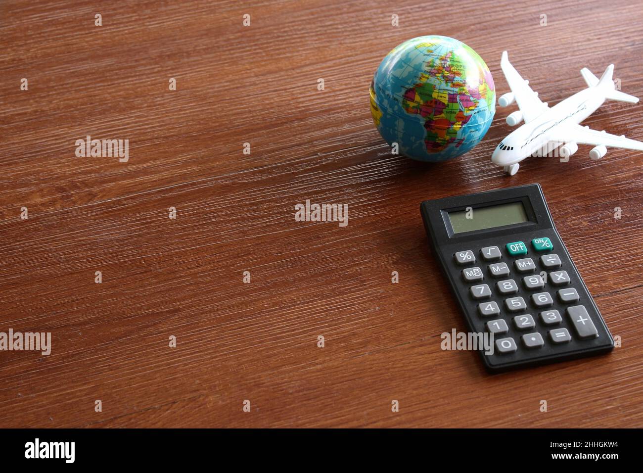 Concetto di calcolo dei costi di viaggio. Piano giocattolo, globo terrestre e calcolatrice su tavola di legno. Foto Stock