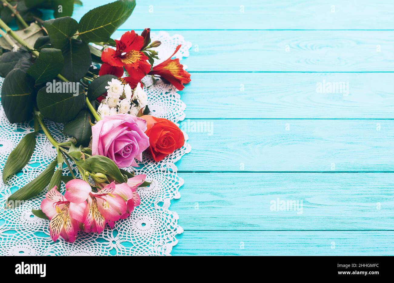 Cornice di fiori e tovaglia di pizzo su sfondo blu in legno. Vista dall'alto e messa a fuoco selettiva. Foto Stock