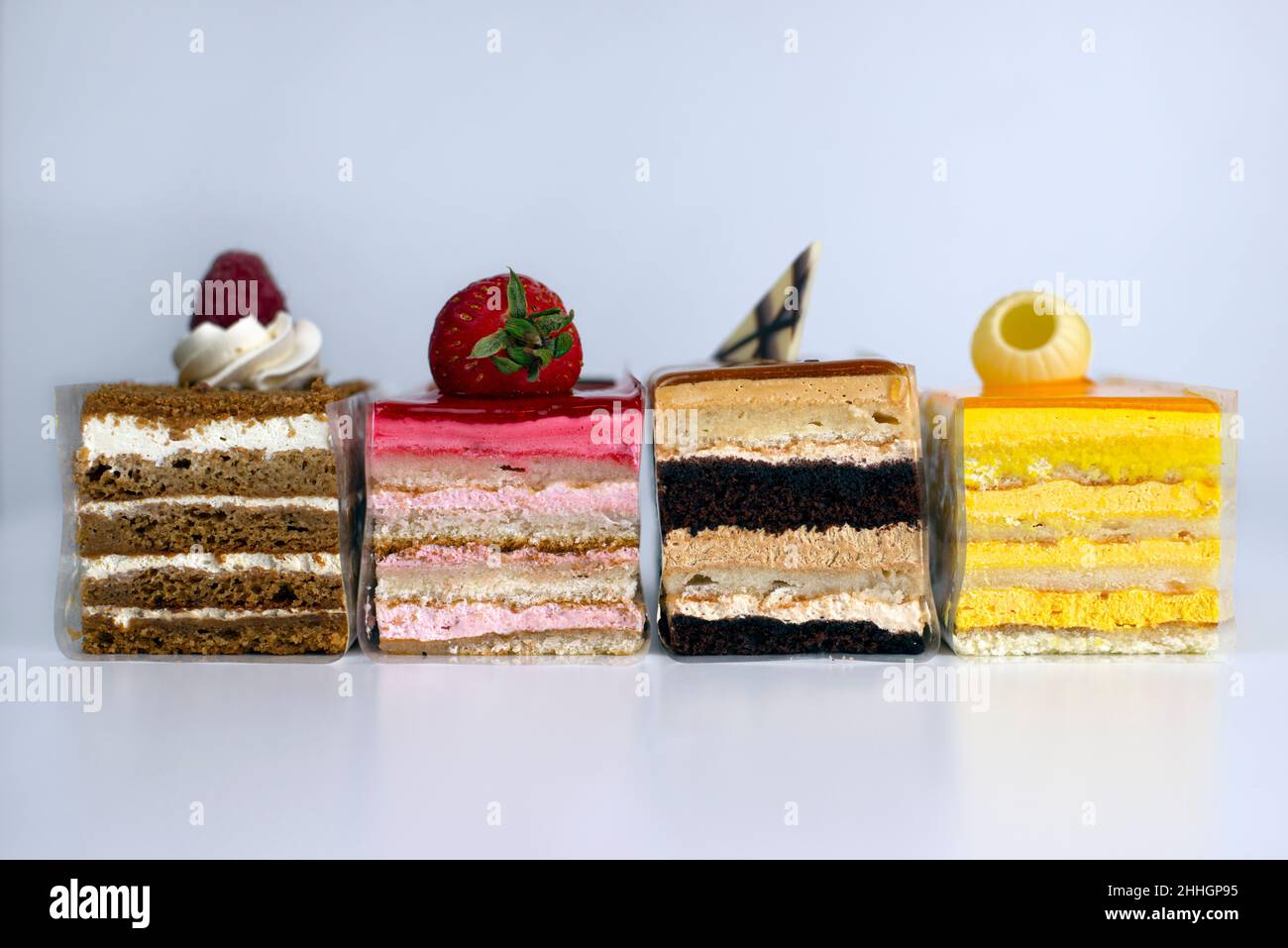 Selezione colorata di fette di torta stratificate su sfondo bianco Foto Stock