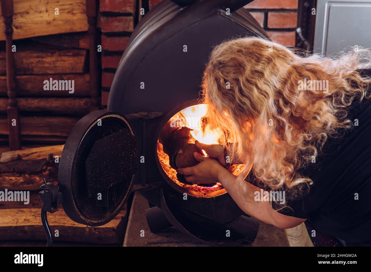 La donna riscalda la stufa di Bullerjan. Home legna bruciare stufa  riscaldamento dispositivo in casa interno, con pila di legna accanto ad  esso Foto stock - Alamy