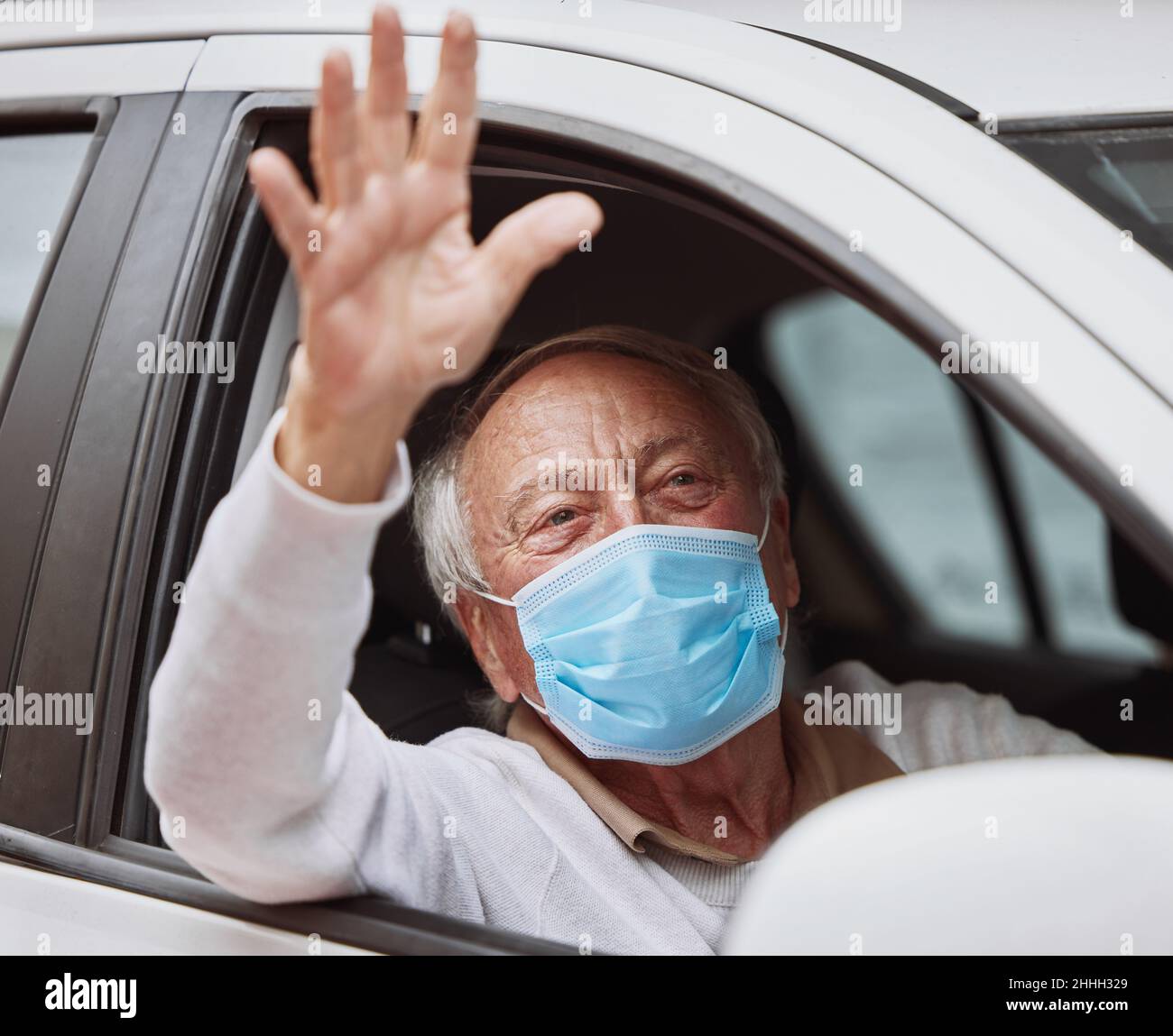 Si è trattato di un processo rapido. Colpo di un uomo anziano che ondula mentre si siede nella sua automobile ad un azionamento attraverso il luogo di vaccinazione. Foto Stock