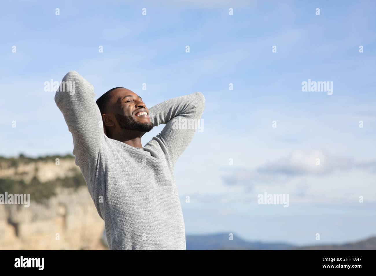 Uomo rilassato con pelle nera che respira aria fresca con le mani sulla testa in montagna Foto Stock