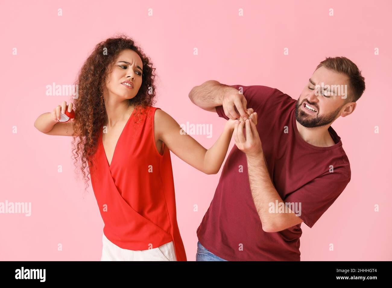 Il giovane uomo che cerca di prendere l'impegno suona il dito della sua ragazza dispiaciuti per forza su sfondo a colori Foto Stock