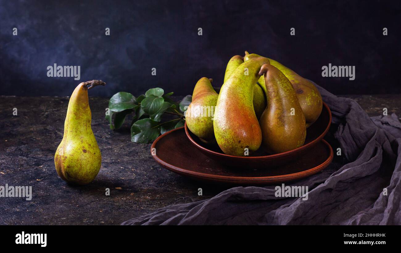 Vita rurale morta, fotografia oscura a basso tasto - vista di una conferenza pera in piatti di argilla, primo piano con fuoco selettivo Foto Stock