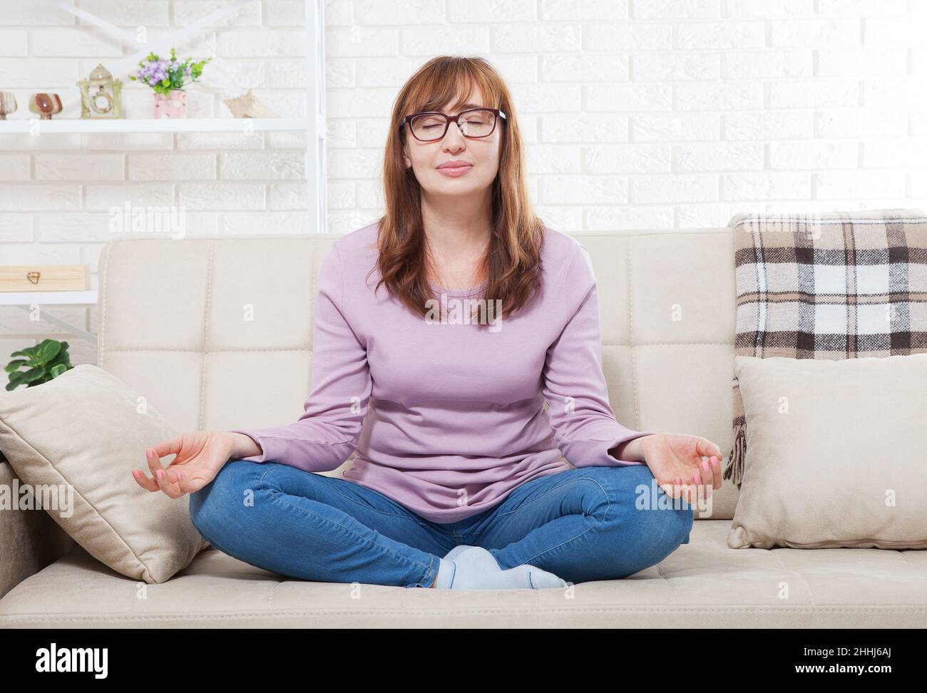 Donna che fa yoga a casa in camera da letto. Meditating femminile di mezza età in ambienti chiusi. posa yoga. Stile di vita e concetto di menopausa Foto Stock