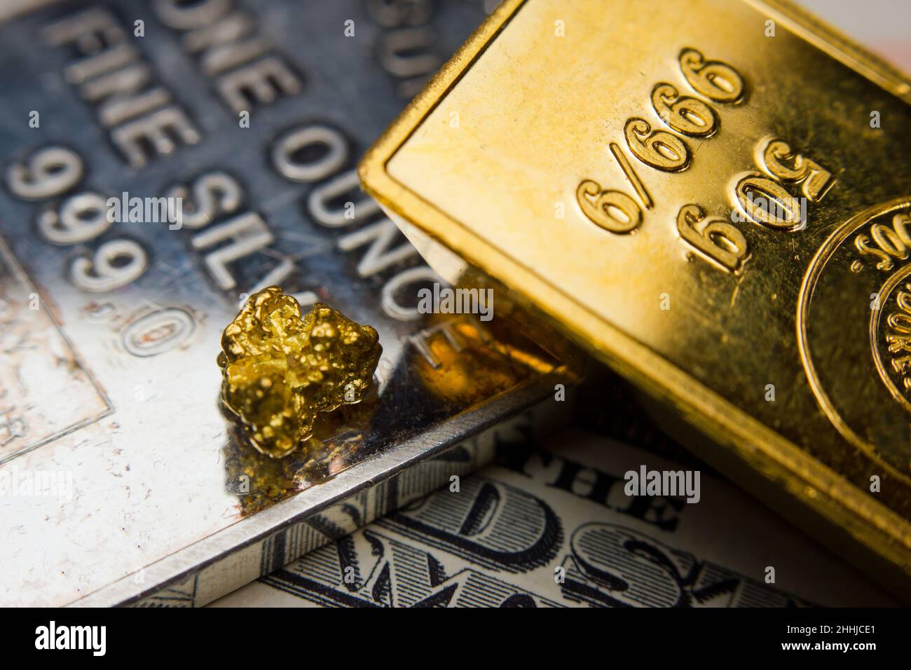Primo piano di un lingotto d'oro e di un nugget d'oro in cima a un'oncia d'argento troy e banconote statunitensi Foto Stock