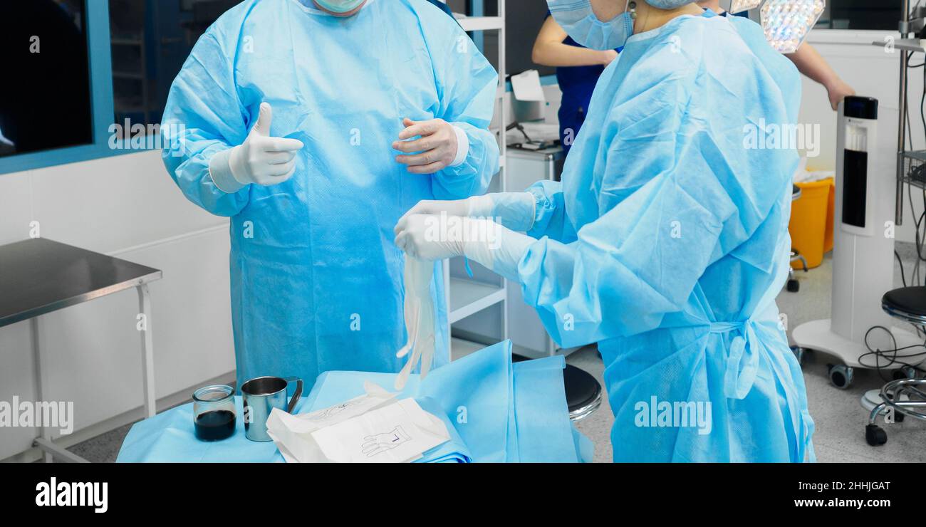 I medici in uniformi chirurgiche indossano guanti sterili prima di iniziare l'intervento chirurgico. Foto Stock