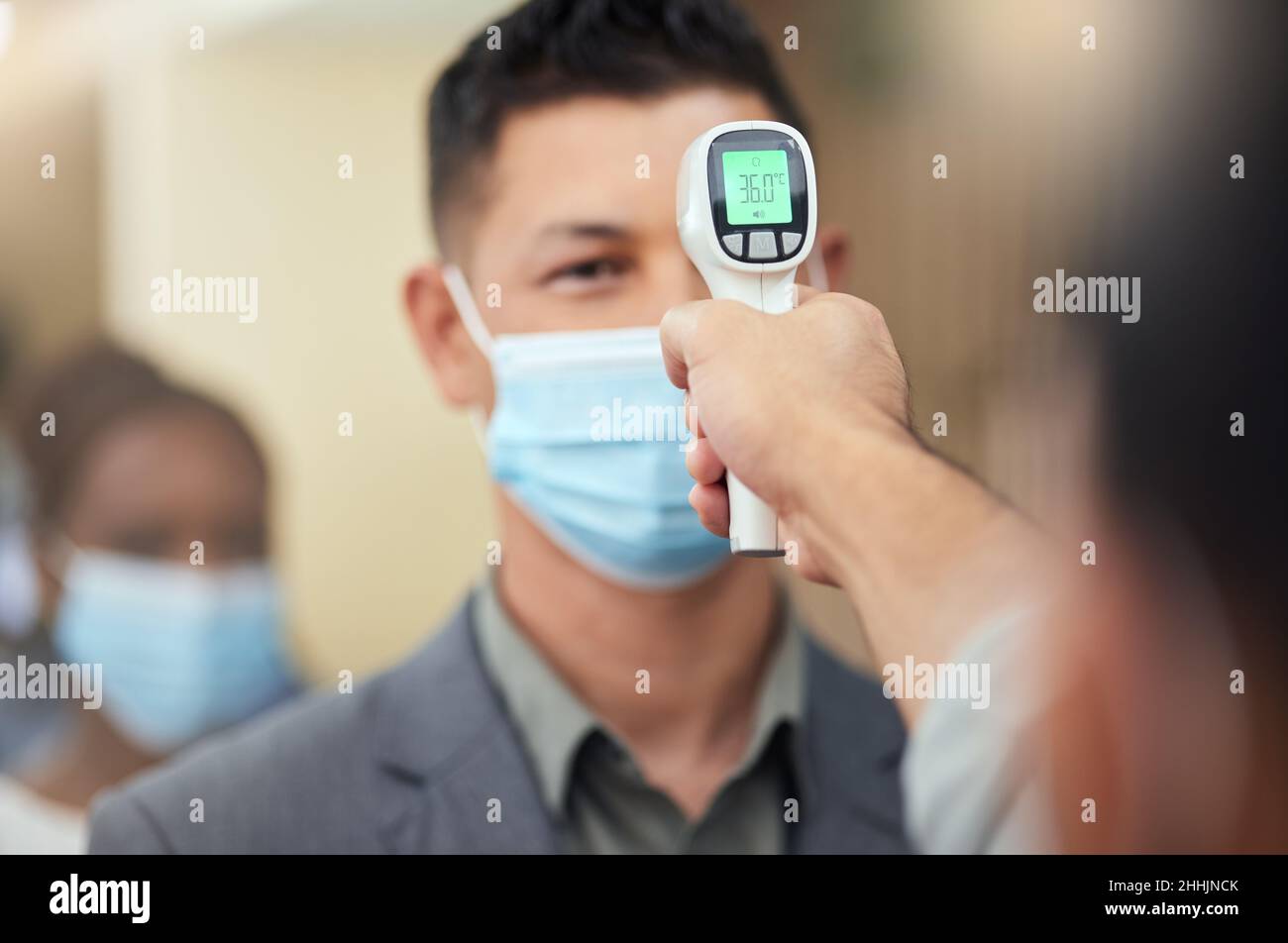 È la nuova normalità. Scatto corto di un bel uomo d'affari maturo che indossa una maschera e che ha la sua temperatura presa mentre sta in piedi alla testa di un Foto Stock