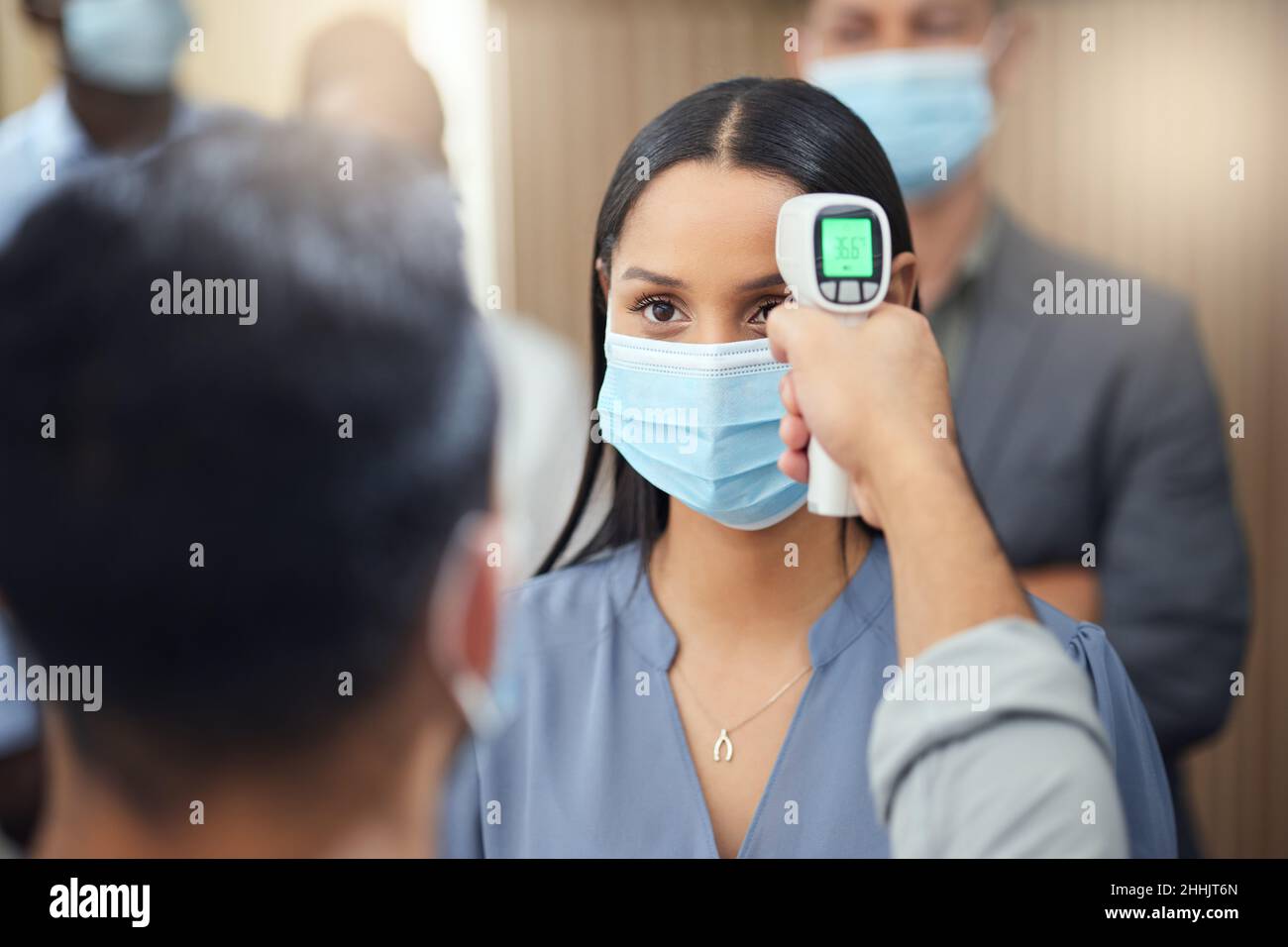 Permettetemi di ottenere la vostra temperatura. Scatto corto di una giovane donna d'affari attraente che indossa una maschera e che ha la sua temperatura presa mentre in piedi a. Foto Stock