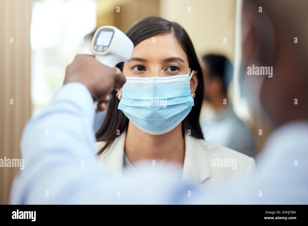 Ogni dipendente deve essere sottoposto a screening. Scatto corto di una giovane donna d'affari attraente che indossa una maschera e che ha la sua temperatura presa mentre in piedi Foto Stock