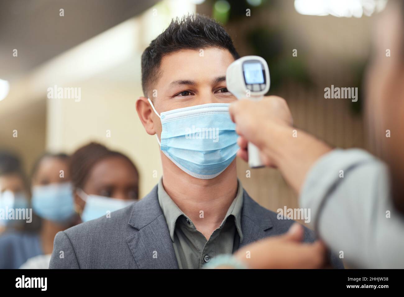 Passando attraverso lo screening covid. Scatto corto di un bel uomo d'affari maturo che indossa una maschera e che ha la sua temperatura presa mentre sta in piedi al Foto Stock