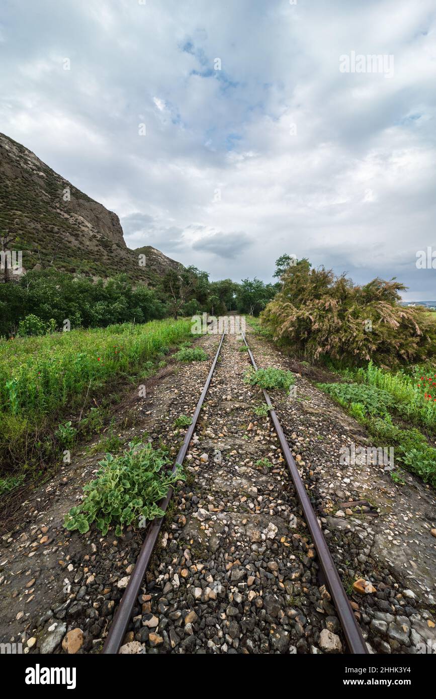Ferrovia diritta che attraversa il paesaggio rurale erboso e le alte colline sotto il cielo nuvoloso Foto Stock