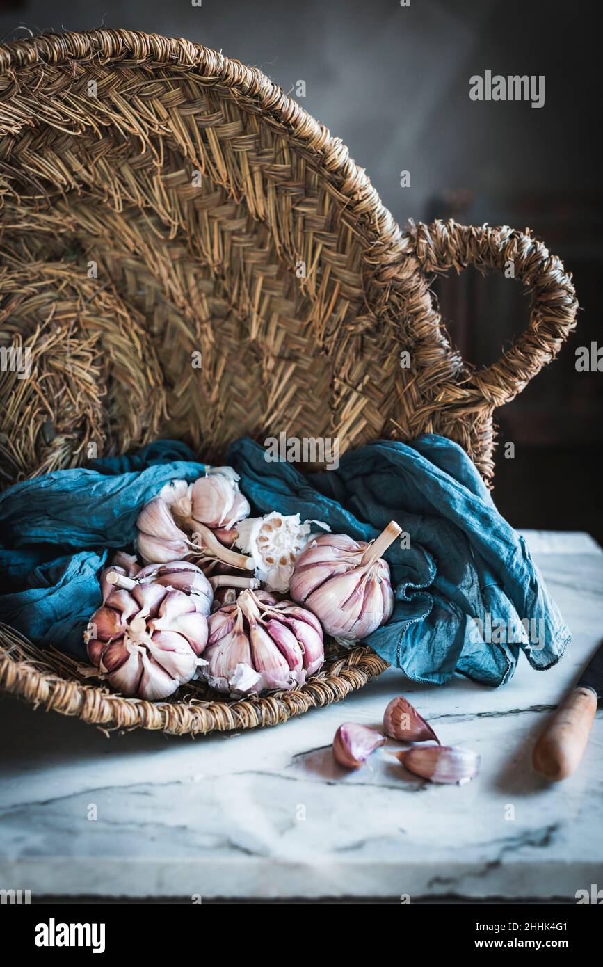 Spicchi di aglio non pelato serviti con tovagliolo blu in un cestino di rattan rotondo posto sul tavolo in cucina leggera Foto Stock