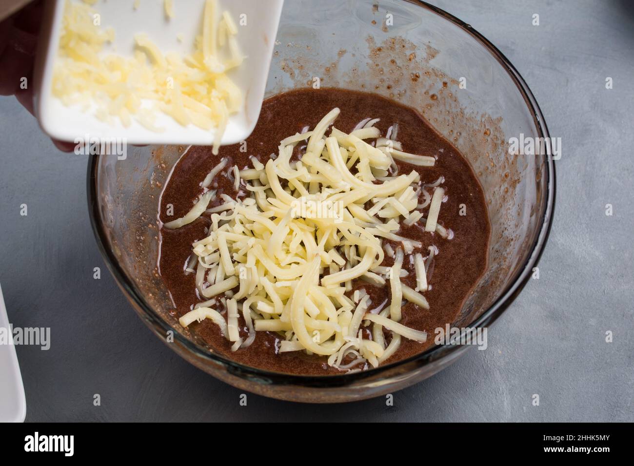Da sopra di raccolto anonimo cuoco aggiungendo il burro grattugiato in ciotola con la pastella di cialda dolce di cioccolato durante il processo di cottura in cucina Foto Stock