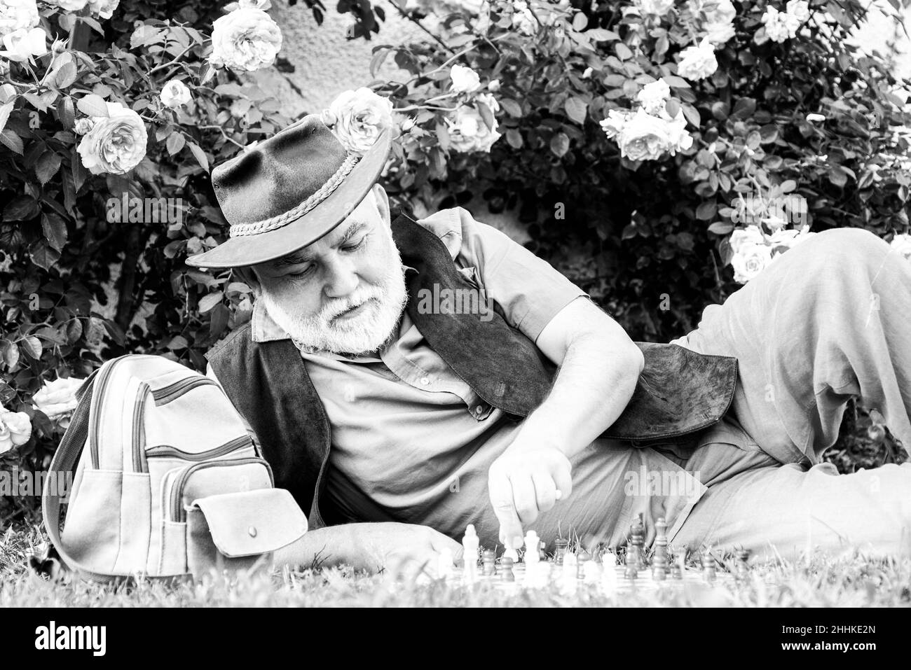 Parco primaverile. Uomo maturo che si rilassa in giardino. Il giardiniere senior gioca a scacchi all'aperto. Foto Stock