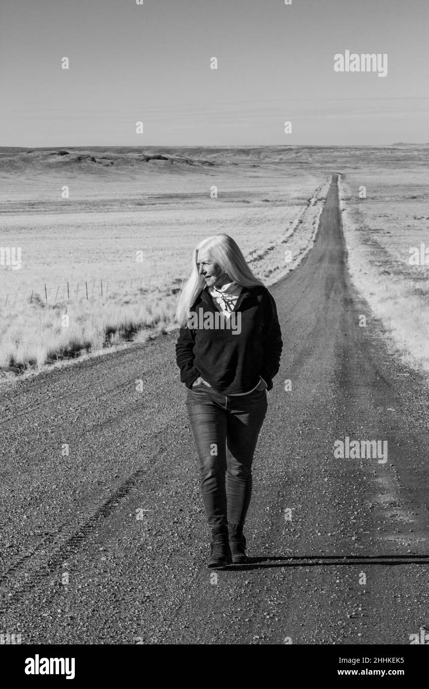 USA, Nevada, Winnemucca, donna anziana che cammina lungo la strada del deserto Foto Stock