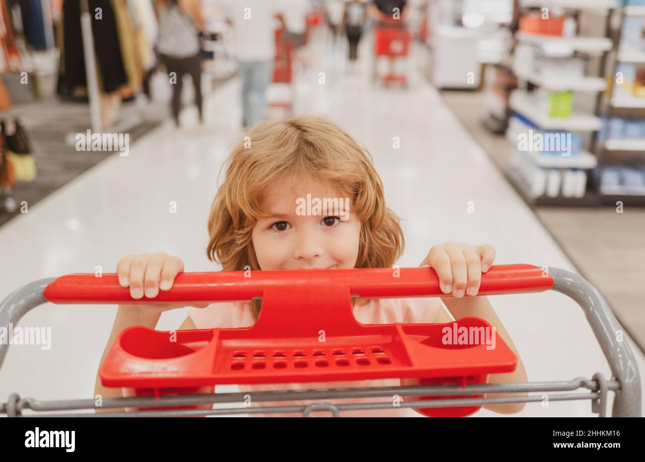 Primo piano ritratto di bambino con carrello di acquisto di cibo in un negozio di alimentari. I clienti della famiglia che acquistano i prodotti al supermercato. Faccia divertente dei bambini. Foto Stock