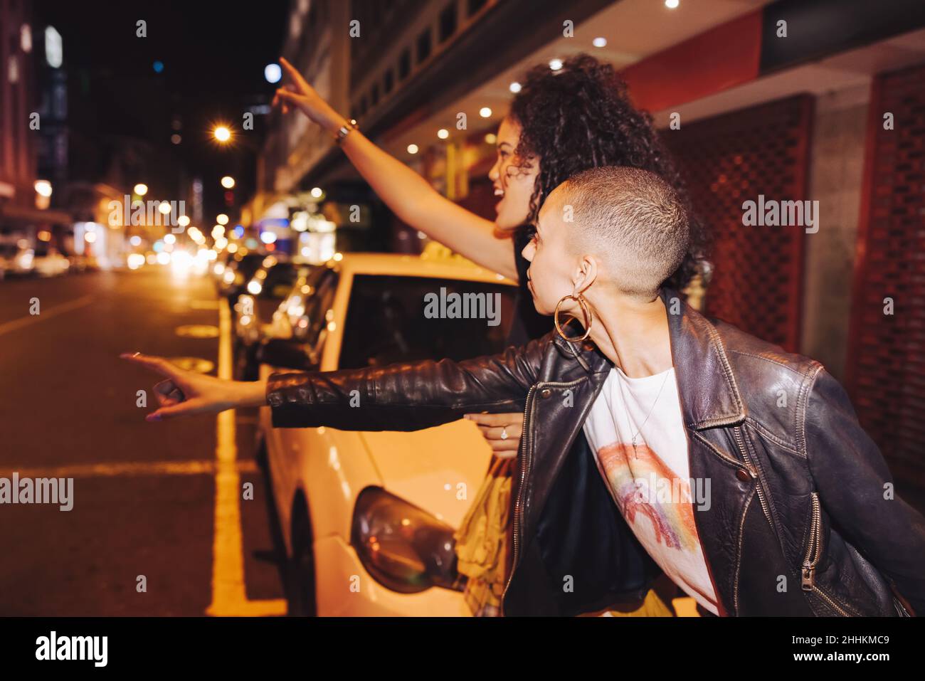 Due giovani amici femminili che salutano un taxi mentre si trovano in piedi lungo la strada della città. Due giovani donne che escono insieme il fine settimana. Girlfriends cal Foto Stock