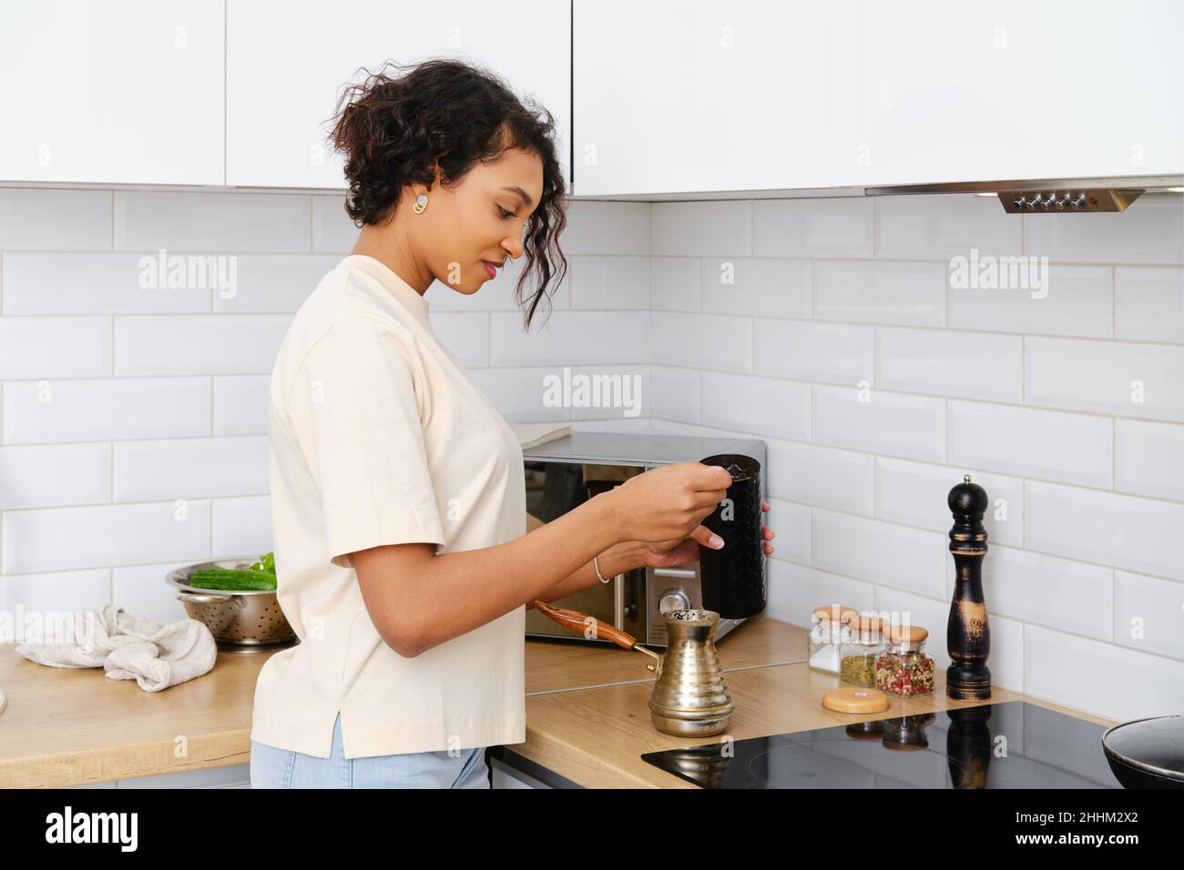 Sonnolenta donna afroamericana che fa caffè macinato a casa in cezve turco Foto Stock