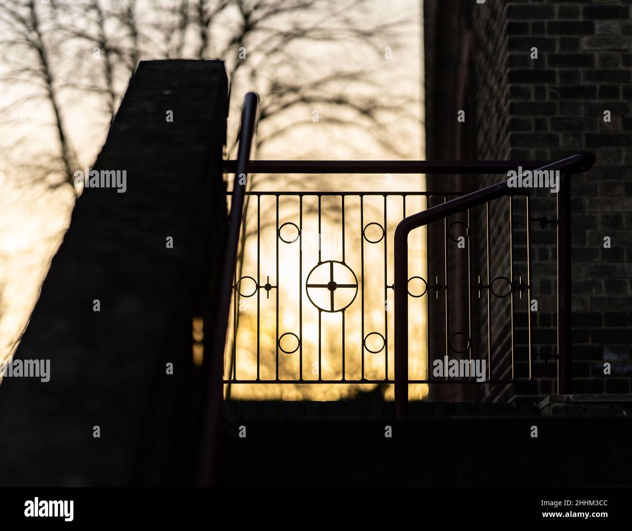 Sole posto dietro la porta della chiesa con crocefisso simbolo in ringhiere metalliche. Bellissimo tramonto arancione dorato. Foto Stock
