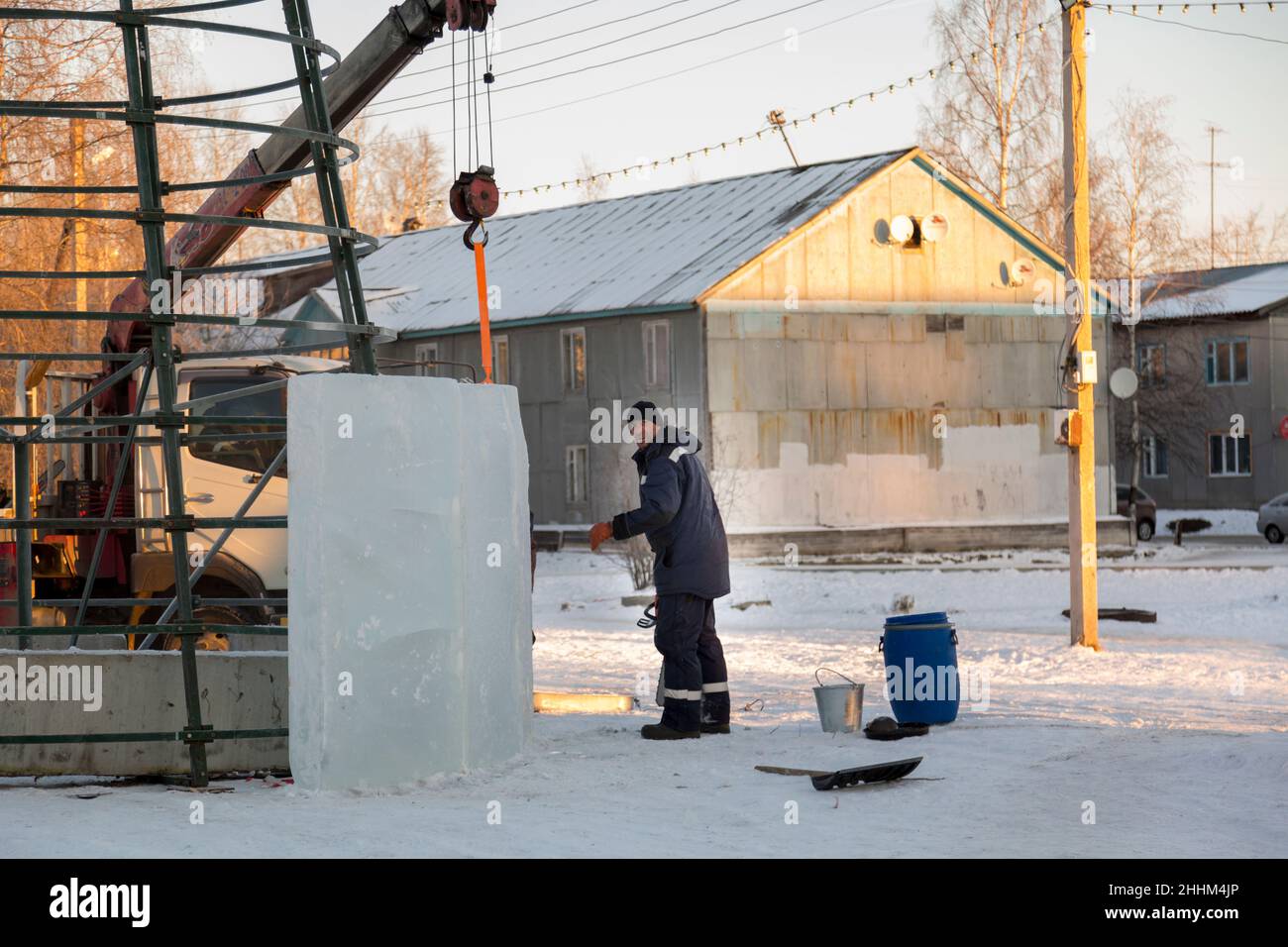 Un costruttore di città di ghiaccio in una giacca blu racchiude un albero di Natale in costruzione con pannelli di ghiaccio alti Foto Stock