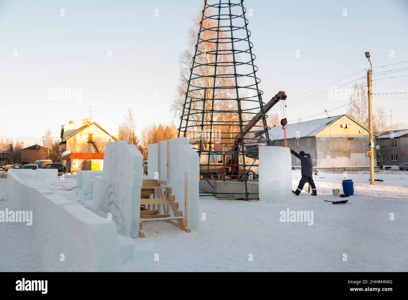 Un costruttore di città di ghiaccio in una giacca blu racchiude un albero di Natale in costruzione con pannelli di ghiaccio alti Foto Stock