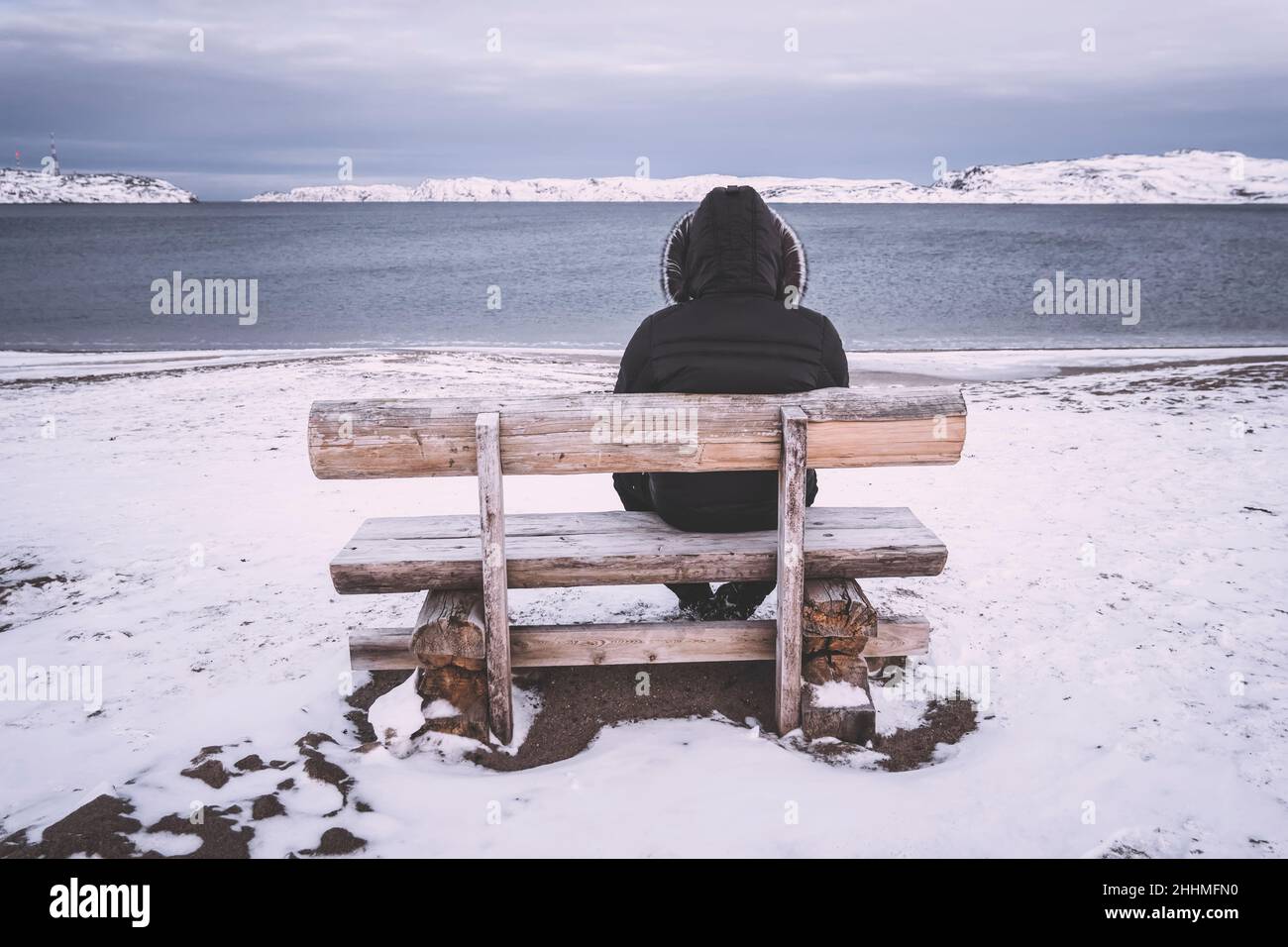 l'uomo vecchio si siede da solo su una panchina sullo sfondo della baia. concetto di solitudine e solitudine. Freddo paesaggio invernale. Un uomo si siede da solo e guarda Th Foto Stock