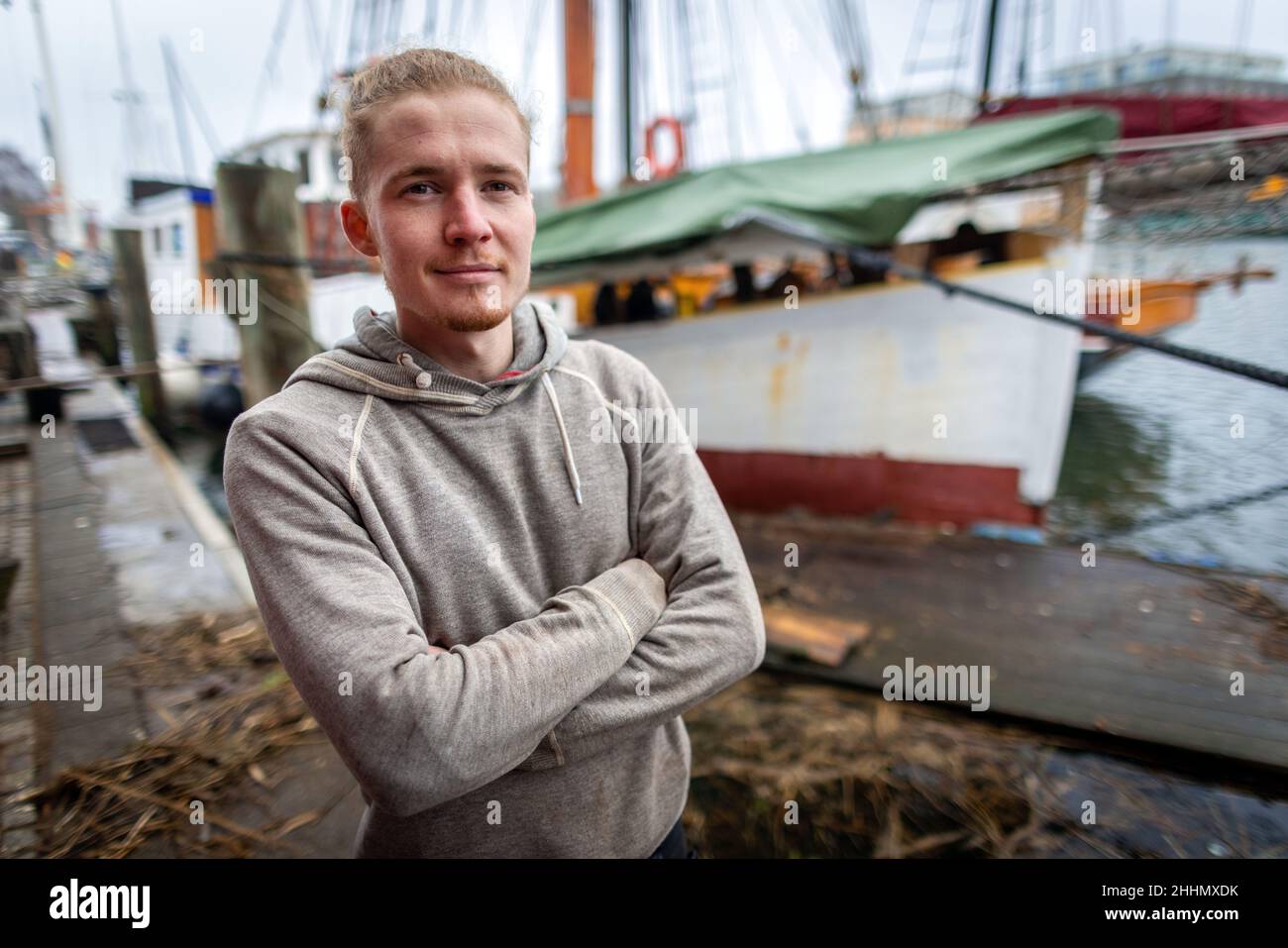 Greifswald, Germania. 25th Jan 2022. Florian Woll, costruttore di imbarcazioni, si erge di fronte al tagliatore di missione 'Elida' costruito nel 1939 presso il cantiere del museo, come l'attuale vincitore nazionale del concorso di artigianato tedesco per i costruttori di imbarcazioni. La Camera dell'artigianato del Meclemburgo-Pomerania occidentale (HWK) aveva precedentemente presentato il certificato e il trofeo presso l'impianto di addestramento Greifswald. Secondo la HWK, 58 società che operano nel settore navale e navale sono registrate nella sua giurisdizione. Credit: Jens Büttner/dpa-Zentralbild/dpa/Alamy Live News Foto Stock