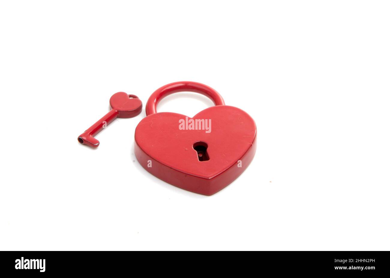 cuore rosso metalico con una chiave sul bianco Foto Stock