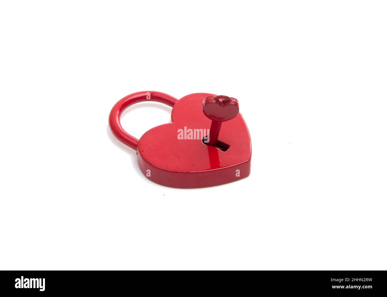 cuore rosso metalico con una chiave sul bianco Foto Stock